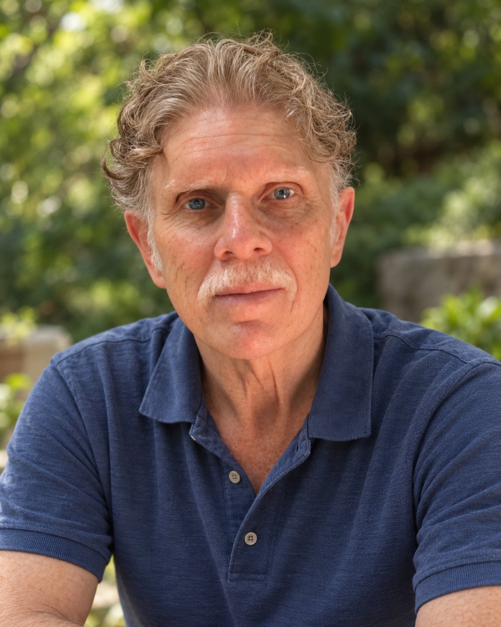 Michael Cassimaty outdoors in a navy polo shirt, with leafy garden behind him